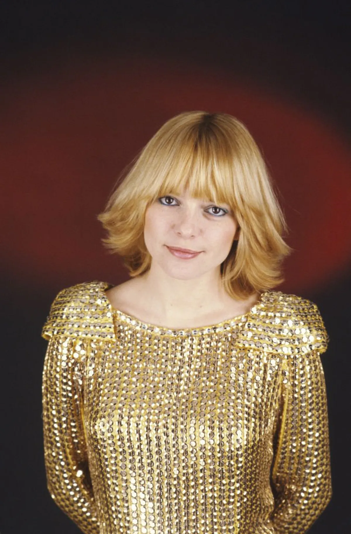 Plan de face souriant de France GALL sur fond rouge, portant le costume doré de son personnage Cristal qu'elle interprête dans l'opéra rock 'Starmania'. | source : Getty Images