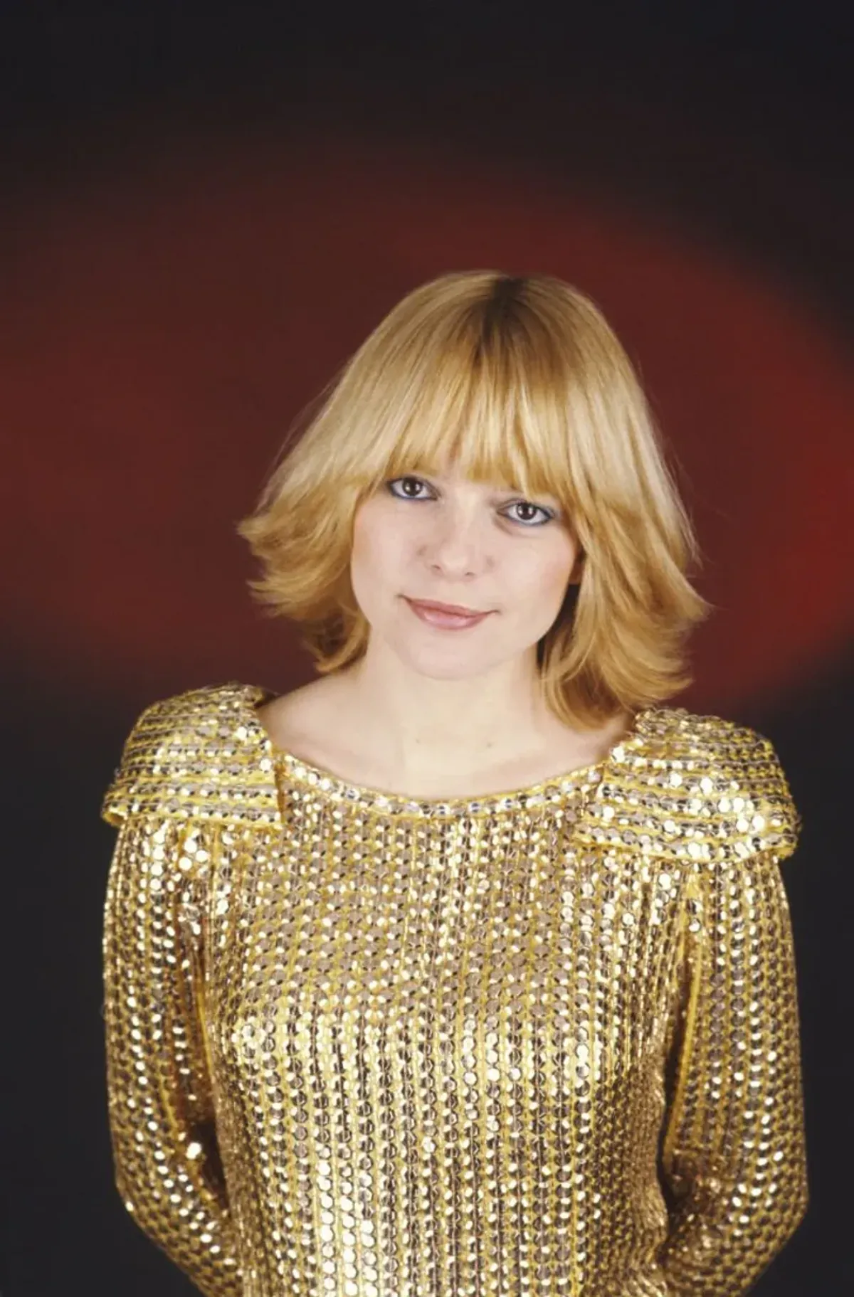 Plan de face souriant de France GALL sur fond rouge, portant le costume doré de son personnage Cristal qu'elle interprête dans l'opéra rock 'Starmania'. | source : Getty Images
