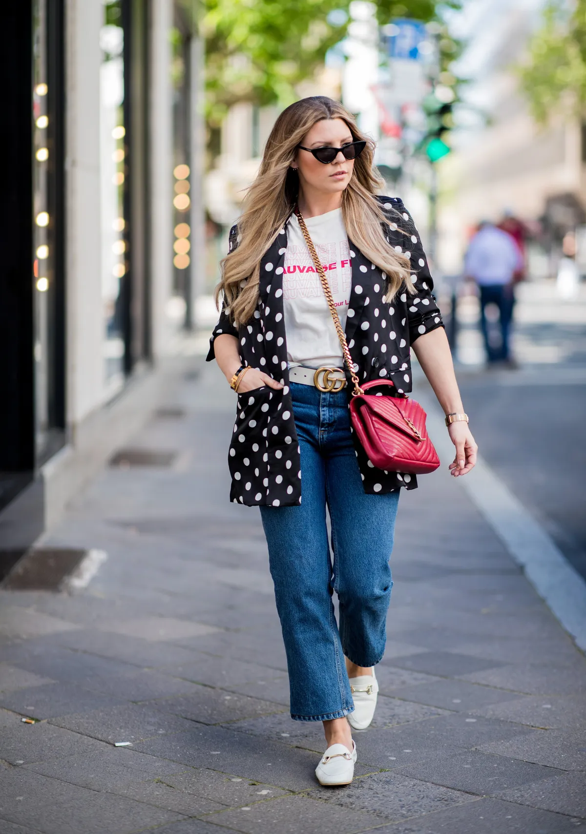 Verena Ahmann porte un blazer long à pois en satin noir blanc de Mango, une chemise rouge beige et un pantalon en jean 7/8 Sincerely Jules, des chaussures de couleur Off White Office London, un sac crossbody rouge doré YSL, une ceinture or crème Gucci, des lunettes de soleil, le 6 mai 2018 à Düsseldorf, en Allemagne | Photo : Getty Images