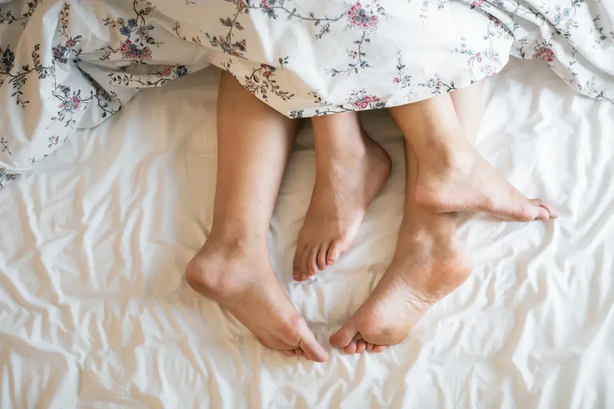 Des jambes d'adultes dépassant d'une couette. | Photo : Pexels